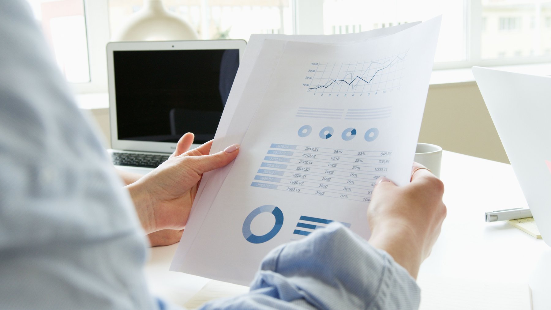 An investor reading a printed report at a desk, papers and a pen beside it