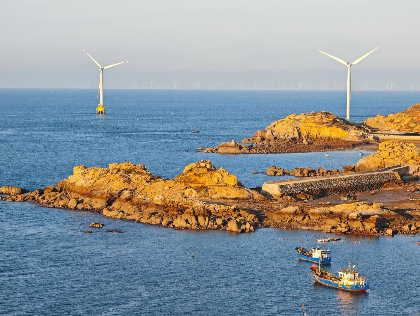 Offshore wind turbines beyond a rocky coastline at low sun