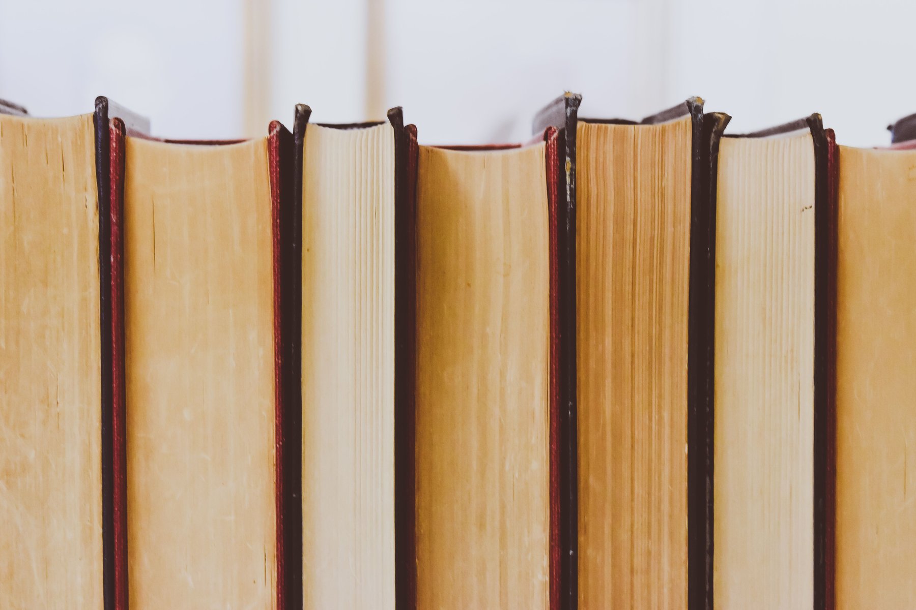 A close-up row of hardback books stood upright, their yellowed page edges facing out between dark red and black spine boards
