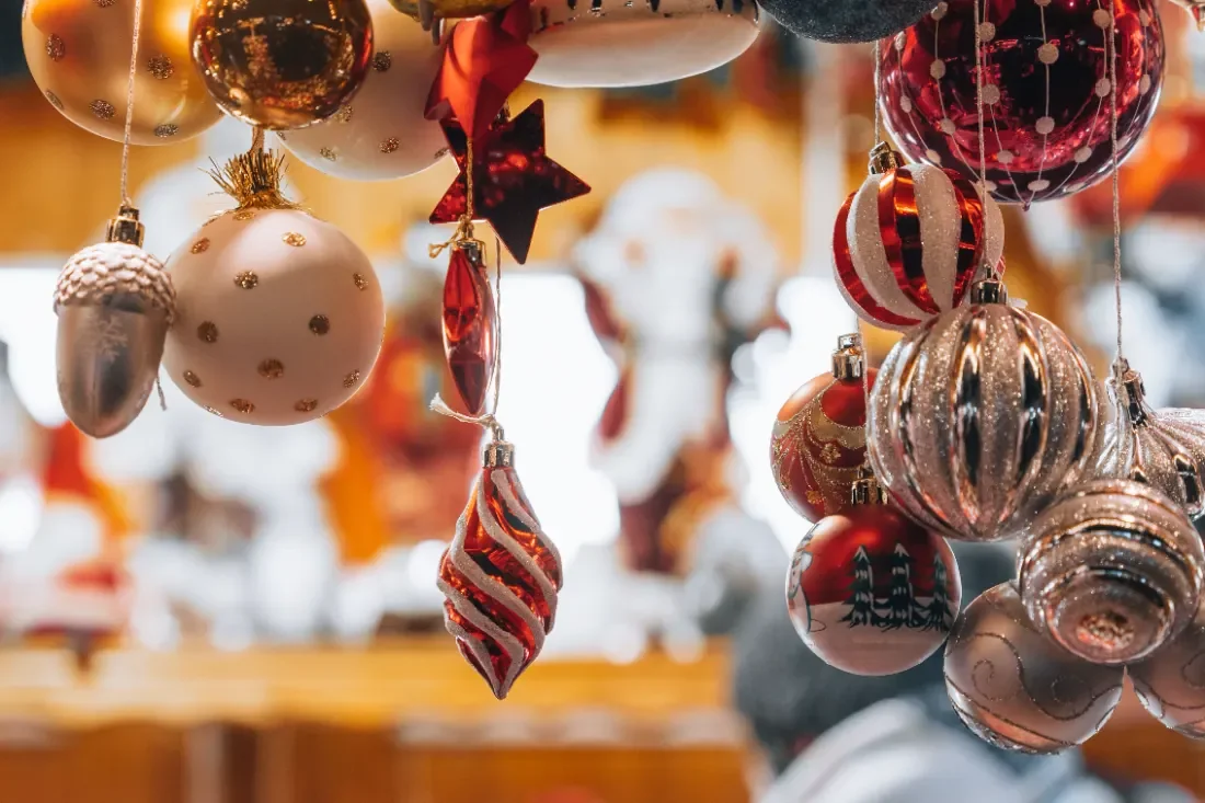 Gold, red and cream glass Christmas baubles hanging close together above a blurred market stall