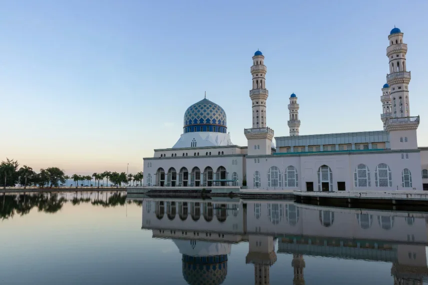 The white Kota Kinabalu City Mosque, its blue-tiled dome and minarets mirrored in the still lagoon at dusk
