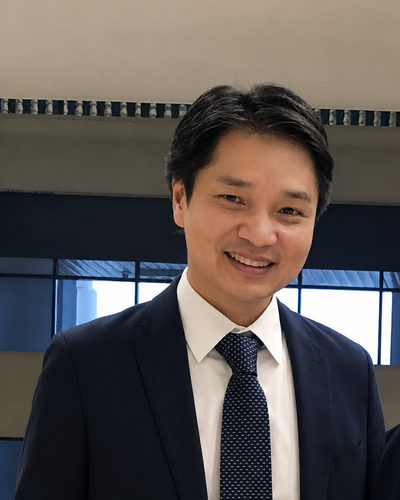 Portrait of YB Datuk Roger Chin in a dark suit and patterned tie, photographed indoors